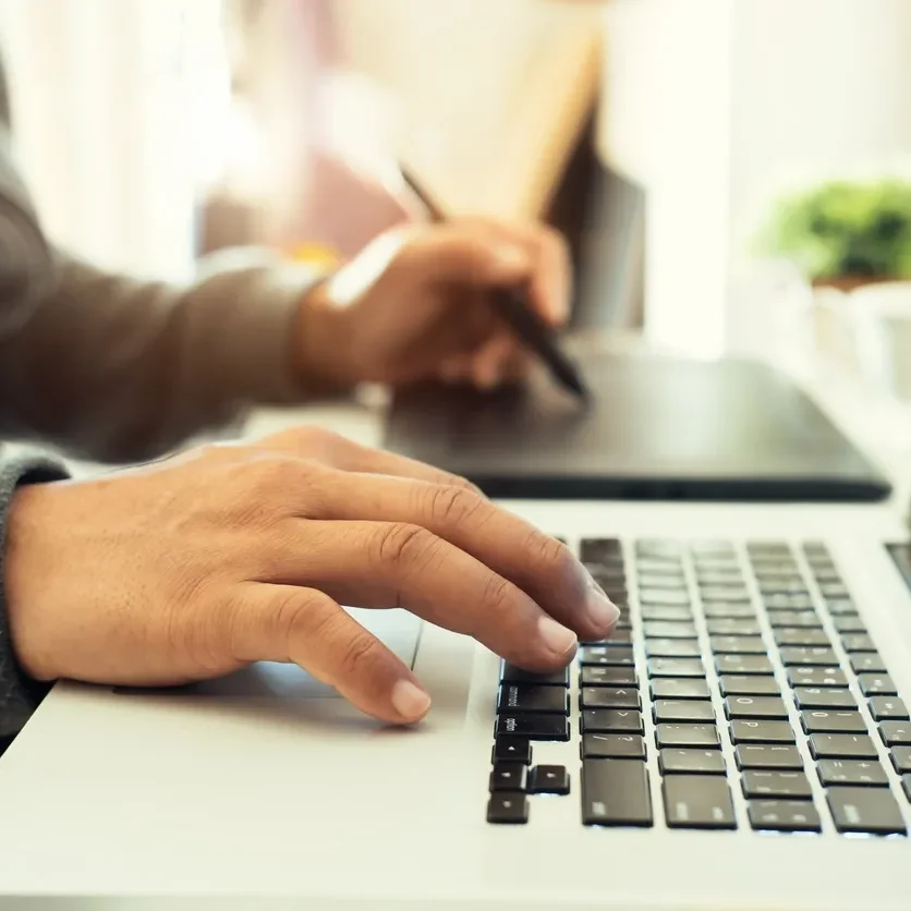 Person working on a laptop with a pen and tablet nearby.