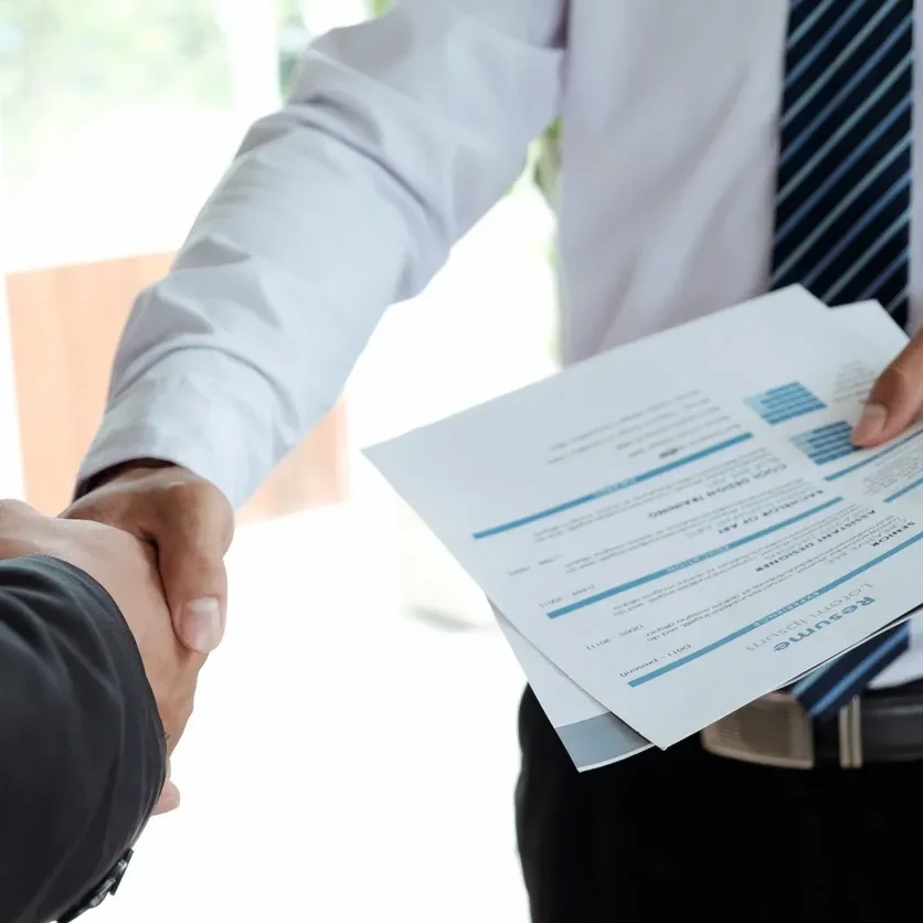 Two people shaking hands during a job interview with a resume in hand.