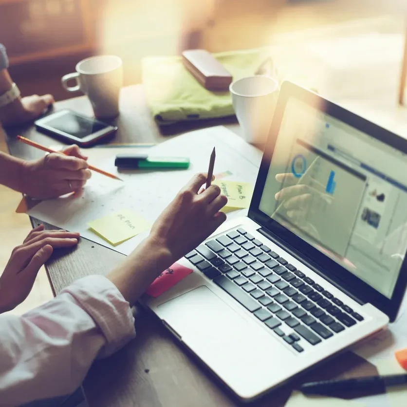 People collaborating on a laptop with notes and charts.